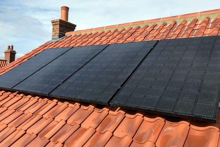 Black solar panels on a roof with orange tiles 