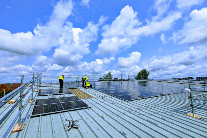 Installers fixing solar panels to a green roof with a cloudy sky above